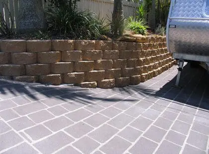 Sandstone block retaining wall beside a charcoal stencilled driveway