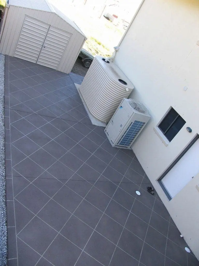 Side yard resurfaced in charcoal diamond tiles beside a water tank