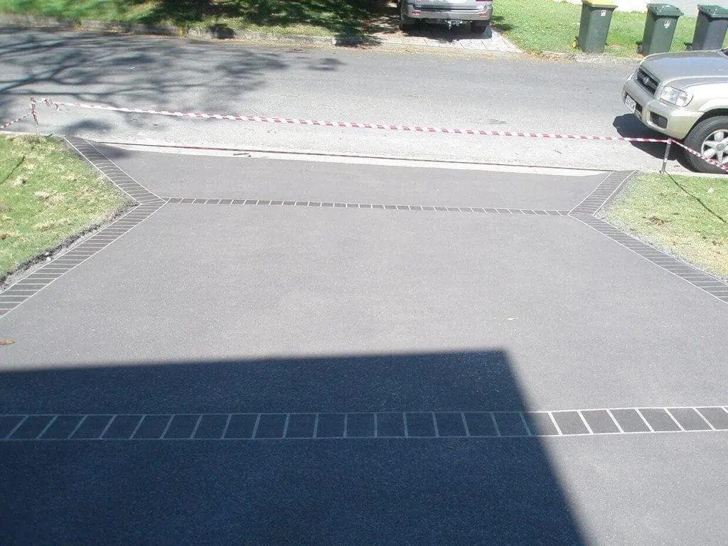 Charcoal concrete driveway resurfacing with a stencilled brick border