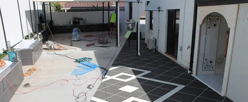 Concrete patio mid-resurfacing, showing the old surface beside the new charcoal tile pattern