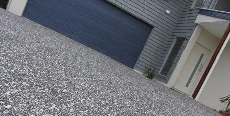 Close view of an exposed aggregate driveway in front of a charcoal garage door