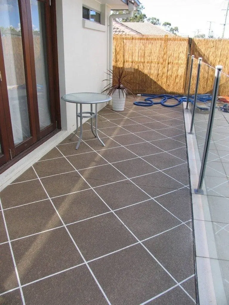 Pool terrace resurfaced in mocha diamond tiles beside glass fencing