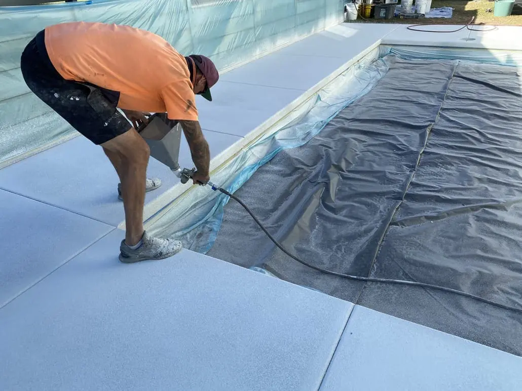 Applicator spraying a resurfacing coat onto a pool surround