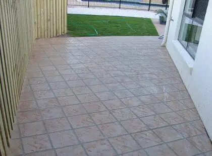 Terracotta tile-stencilled concrete courtyard beside a timber fence